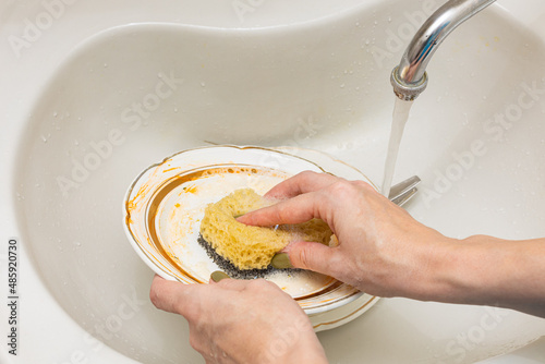 a woman's hand holds a sponge in foam and washes a plate photo