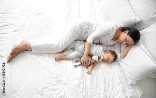 Young mother and her adorable baby with toy sleeping on bed