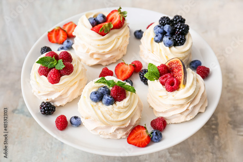 Stand with tasty Pavlova cakes and fresh berries on grunge background