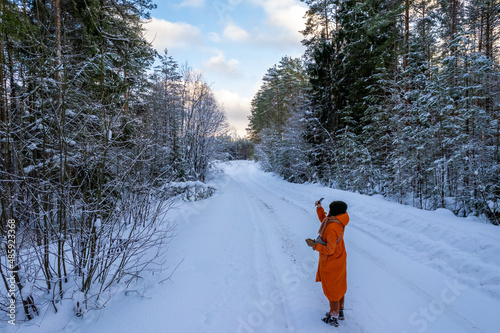 a girl photographs a winter forest in an orange jacket with a dog for a walk in the forest. High quality photo