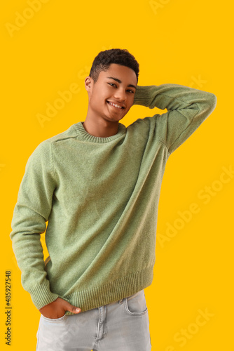 Handsome African-American guy in knitted sweater on yellow background © Pixel-Shot