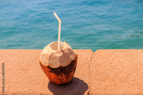Fresh tropical coconut cocktail with drinking straw by ocean