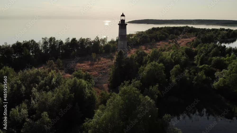 Small island at large lake with old lighthouse, aerial shot. Camera fly back from building and reveal general view on isle. Calm Ladoga waters around, dark image in contrast sun light Small island at large lake with old lighthouse, aerial shot. Camera fly back from building and reveal general view on isle. Calm Ladoga waters around, dark image in contrast sun light