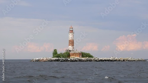 Picturesque lighthouse on tiny stony artificial island, pale colors of picture. Many sea gulls live at uninhabited islet, fly around abandoned place. Pink clouds on background photo