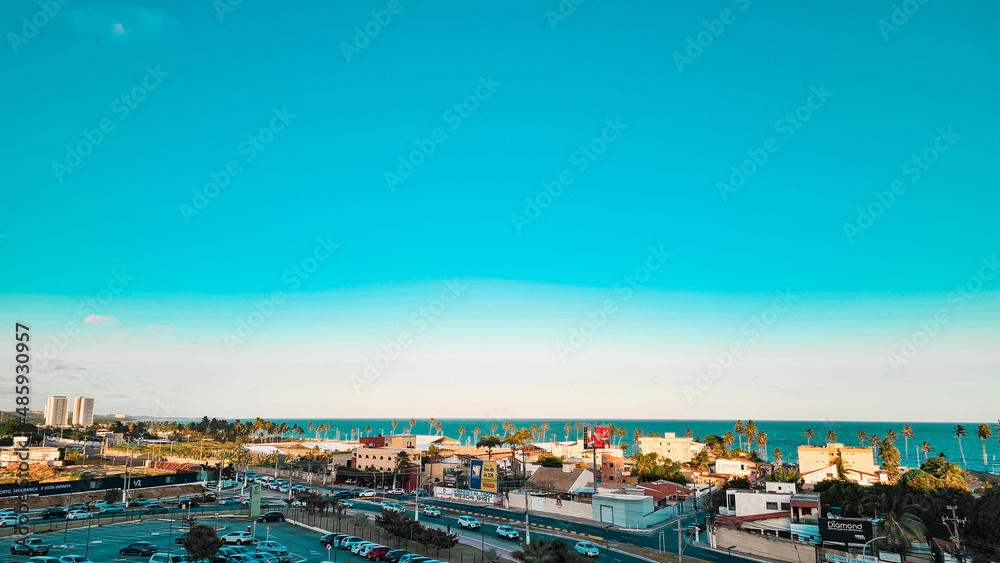 A clean blue sky with some small buildings and the ocean behind.