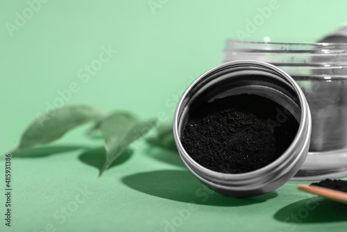 Jar with activated charcoal tooth powder on green background  closeup