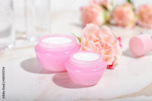 Jars with natural cosmetic cream and flower on light background, closeup