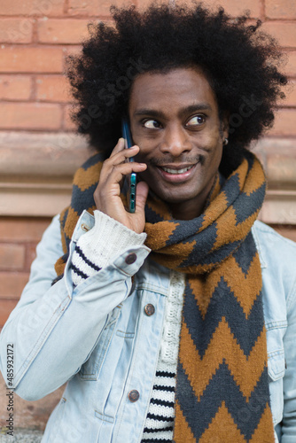 Portrait of young African American man with afro hairstyle and fashionable clothes talking on the phone outdoors. 