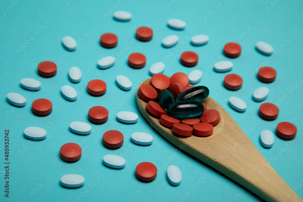 Studio photo of wooden spoon full of medical pills. There are red and light blue pills surrounding the spoon. Studio photo of wooden spoon full of medical pills. There are red and light blue pills surrounding the spoon.