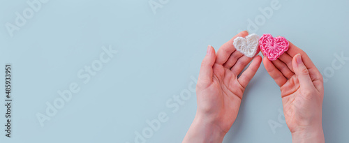 Valentine's day background. Women's hands hold two linked hearts of white and pink color from threads on a blue background. Close-up. The concept of a holiday and relationships. Flat lay, copy space