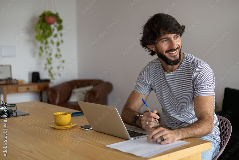 Young business man working at home in his kitchen with laptop and papers on kitchen wooden desk. Home office concept.