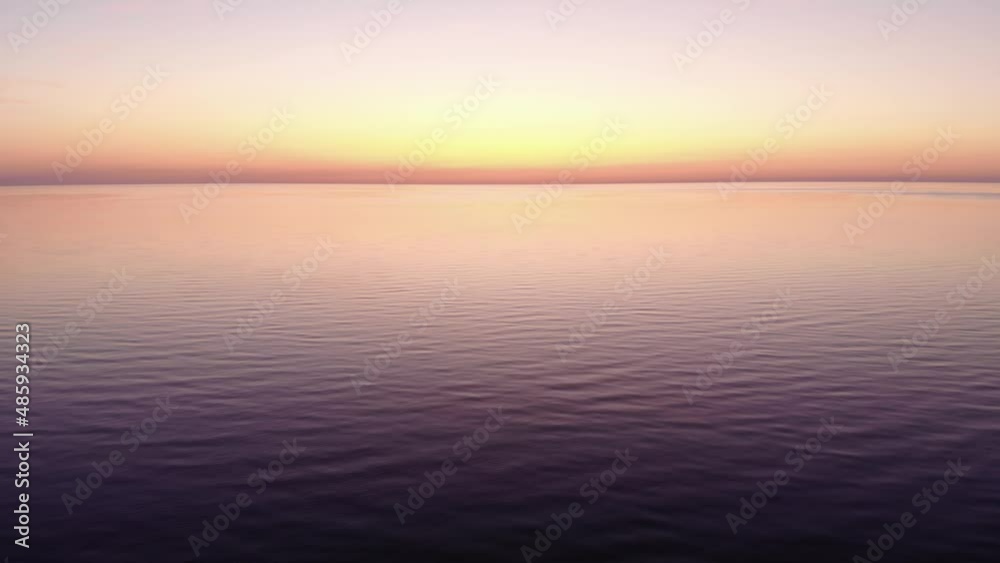 Small waves on calm water of big lake, bright yellow afterglow on clear sky. Aerial shot of Ladoga lake at summer evening, empty water surface until horizon line, neat colors of nature after sunset Small waves on calm water of big lake, bright yellow afterglow on clear sky. Aerial shot of Ladoga lake at summer evening, empty water surface until horizon line, neat colors of nature after sunset