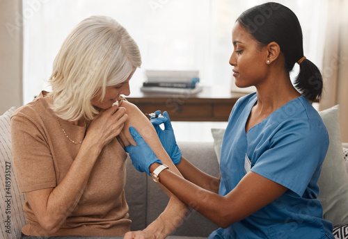 The vaccine that everyones been waiting for. Shot of a doctor giving a senior woman an injection at home.