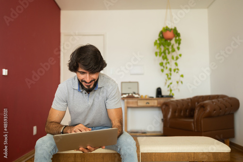 Young business man working at home from his living room chair with laptop on his lap. Home office concept. Gray notebook for working. Home office concept. High quality photo