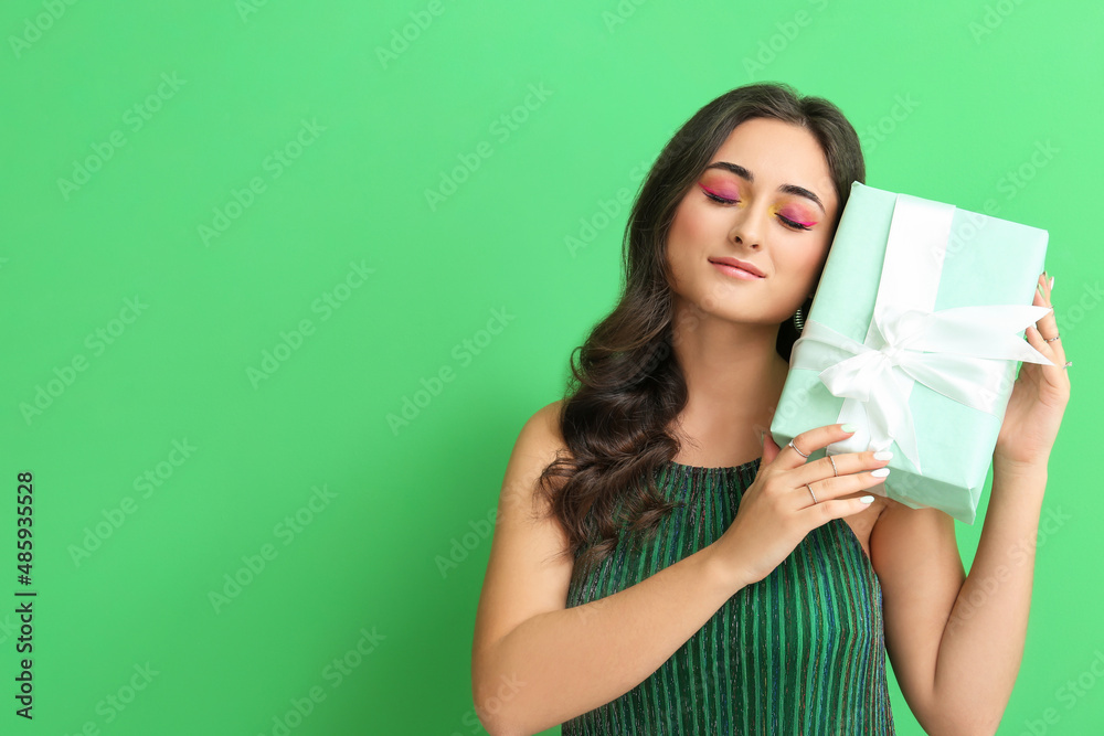 Woman with creative makeup holding gift box on green background. International Women's Day