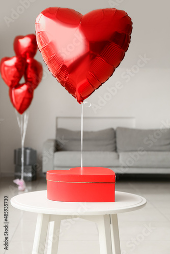Gift box on table and heart shaped air balloon in room decorated for Valentine's day