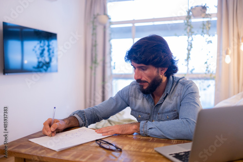 Young business man working at home in his bedroom with laptop and papers on desk. Home office concept.