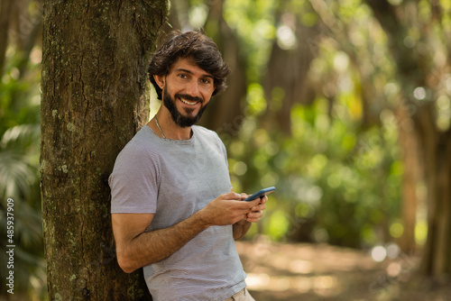 View of young man using a smartphone at day time with a green park in the background. High quality photo