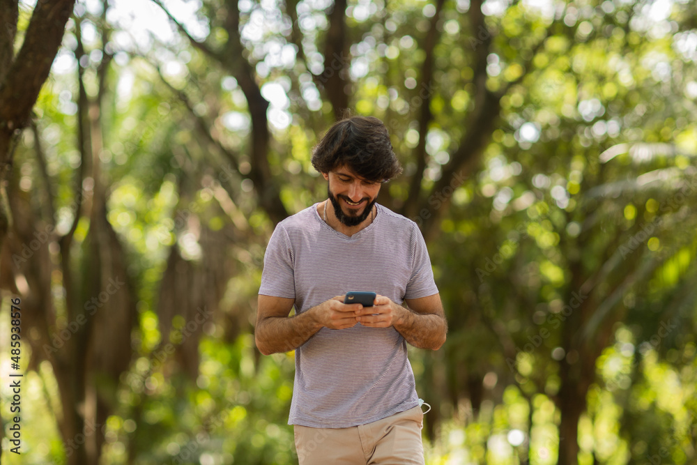 View of young man using a smartphone at day time with a green park in the background. High quality photo View of young man using a smartphone at day time with a green park in the background. High quality photo