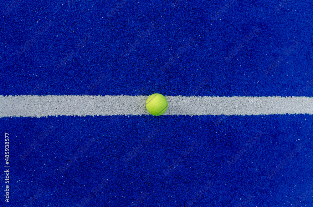 Overhead photo of a ball on the line of a blue synthetic paddle tennis court.