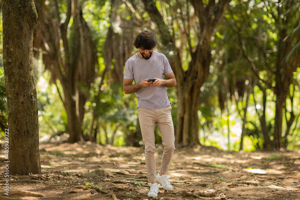 View of young man using a smartphone at day time with a green park in the background. High quality photo