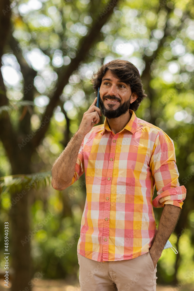 Obraz premium View of young man using a smartphone at day time with a green park in the background. High quality photo