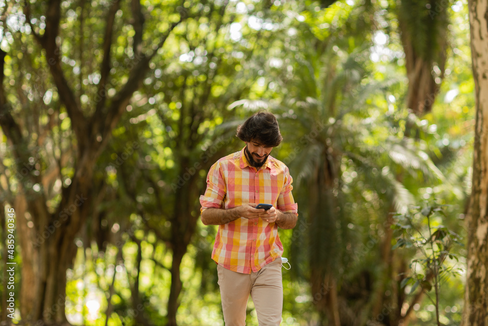 View of young man using a smartphone at day time with a green park in the background. High quality photo View of young man using a smartphone at day time with a green park in the background. High quality photo