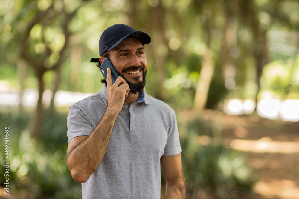 Obraz premium View of young man using a smartphone at day time with a green park in the background. High quality photo
