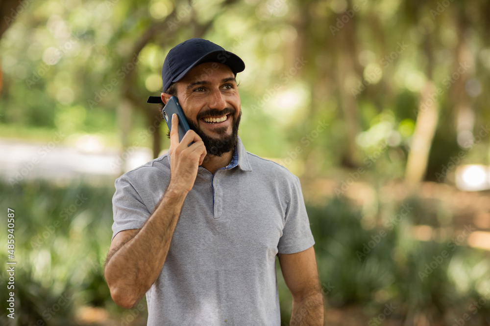 View of young man using a smartphone at day time with a green park in the background. High quality photo