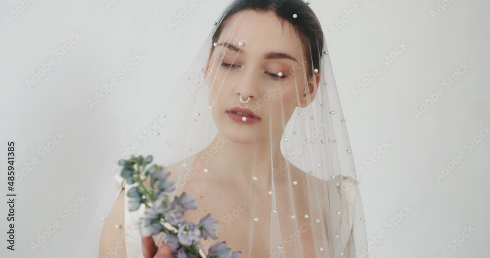 Portrait beautiful young female posing with flowers in her hands standing by clean white wall. Wedding photo session of charming sensual bride under veil. Pretty stylish caucasian woman. Bridal day Portrait beautiful young female posing with flowers in her hands standing by clean white wall. Wedding photo session of charming sensual bride under veil. Pretty stylish caucasian woman. Bridal day
