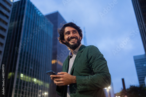 View of young man using a smartphone at night time with city view landscape in the background. High quality photo