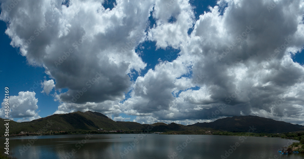 Beautiful lake surrounded by forest and hills under a dramatic sky with foamy clouds and the reflection in water.