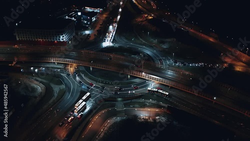 Aerial flyover car traffic roundabout interchange road at night, drone shot top down view expressway intersection in modern city in evening. Cars driving busy junction highway transportation