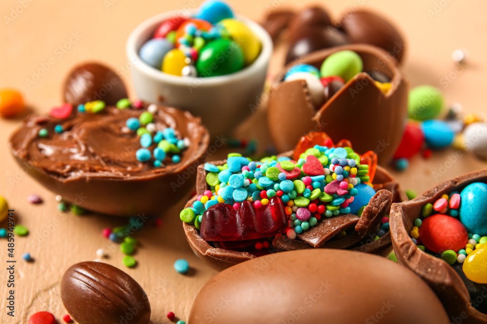 Broken chocolate Easter eggs with different candies and sprinkles beige background, closeup