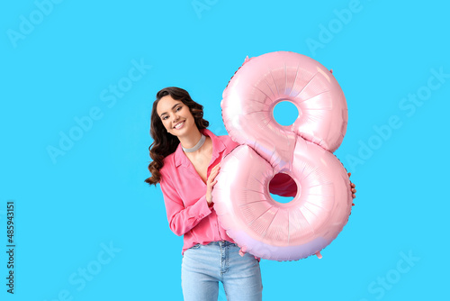 Smiling young woman with big balloon in shape of figure 8 on blue background. International Women's Day