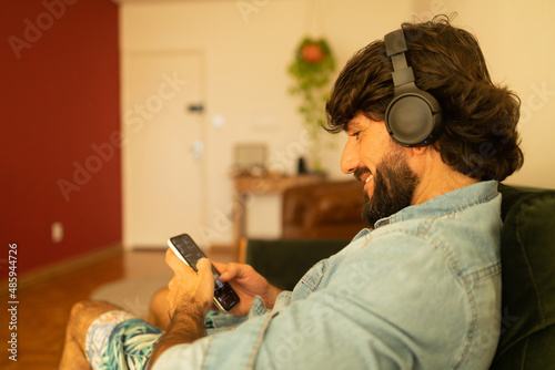 View of young man listening to music with headphones in his ears in the living room of his apartment. High quality photo.