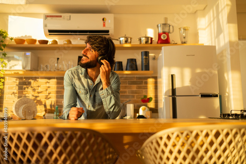 View of young man listening to music with headphones in his ears in the kitchen of his apartment. High quality photo.