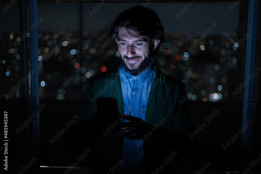 Front view of young man using a smartphone at night time with city view landscape in the background. High quality photo Front view of young man using a smartphone at night time with city view landscape in the background. High quality photo