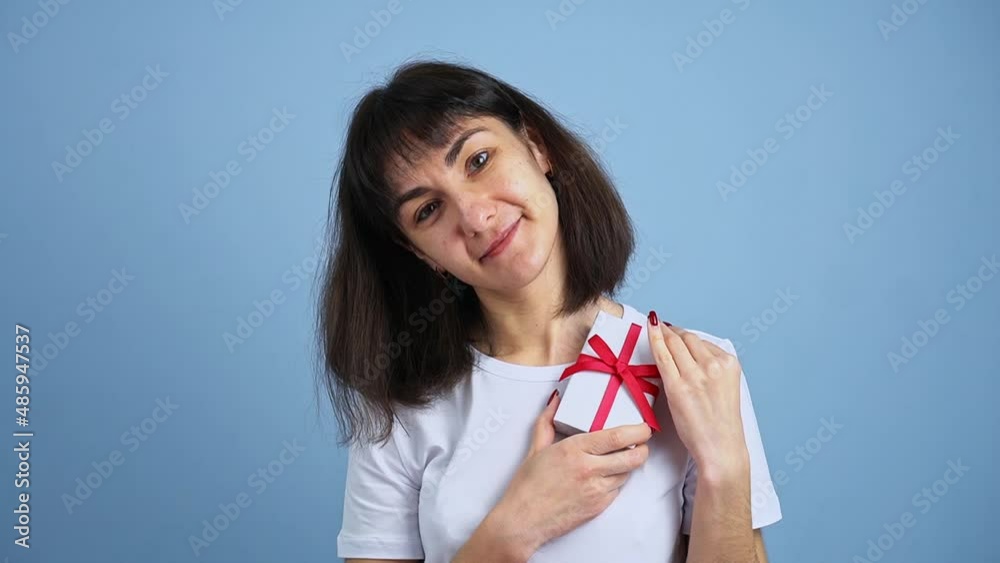 Beautiful smiling woman holding gift box in hand on blue wall background. Girl is happy with present Beautiful smiling woman holding gift box in hand on blue wall background. Girl is happy with present