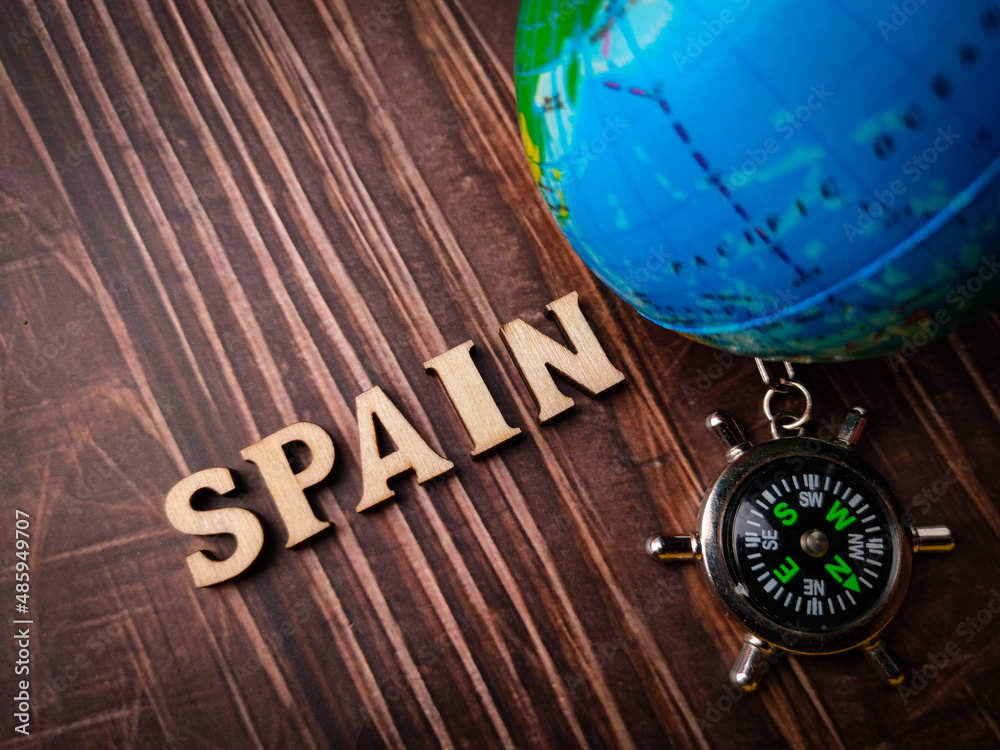 Top view compass,earth globe and wooden word with text SPAIN on wooden background.