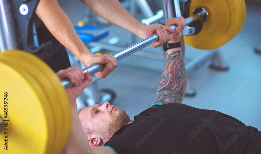 Fototapeta premium Young man lifting the barbell in gym with instructor