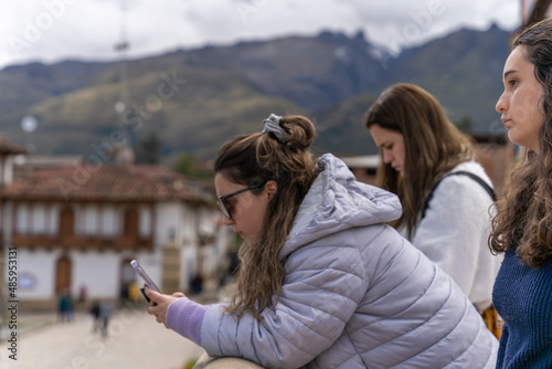 Three girls using the mobile while leaning on a traditional andean bridge photo