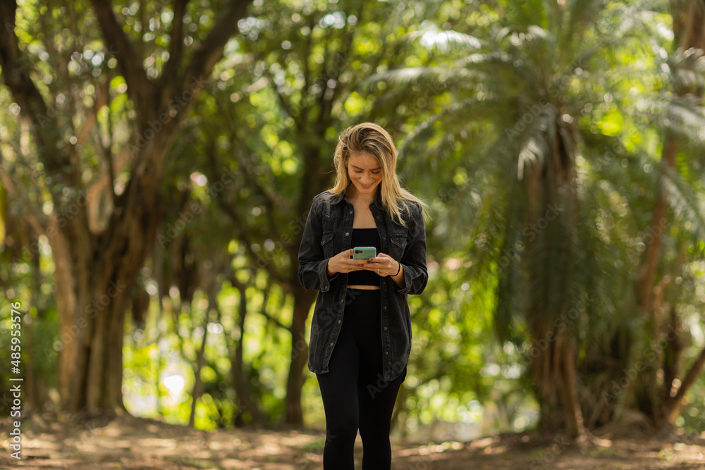 Young woman using a smartphone at day time with a green park in the background. High quality photo Young woman using a smartphone at day time with a green park in the background. High quality photo