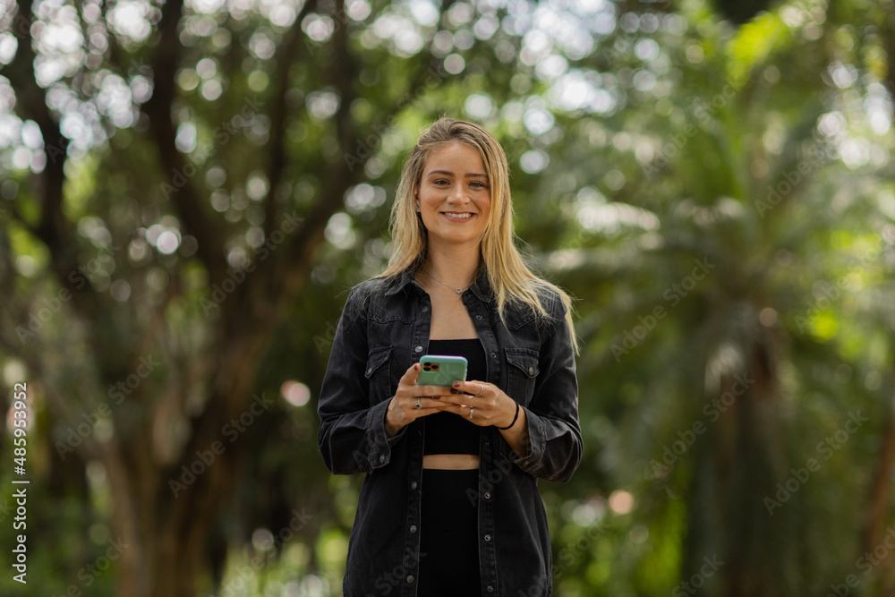Young woman using a smartphone at day time with a green park in the background. High quality photo Young woman using a smartphone at day time with a green park in the background. High quality photo