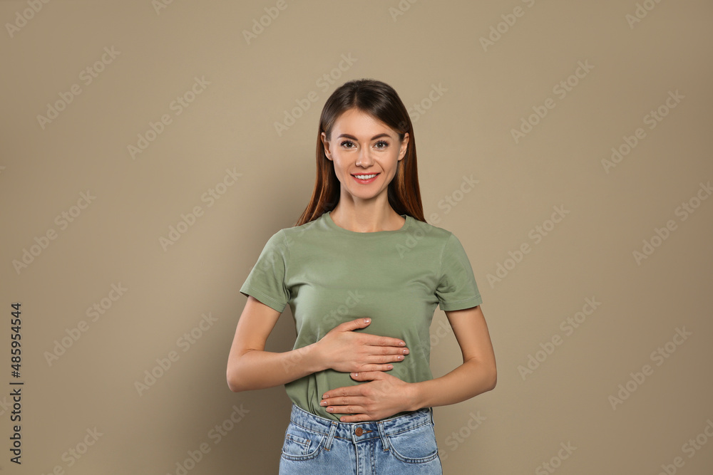 Healthy woman holding hands on belly against beige background - obrazy, fototapety, plakaty 