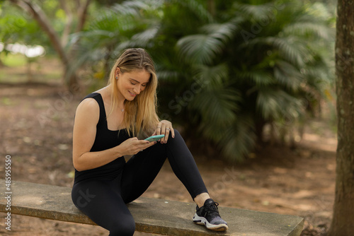 Young woman using a smartphone at day time with a green park in the background. High quality photo