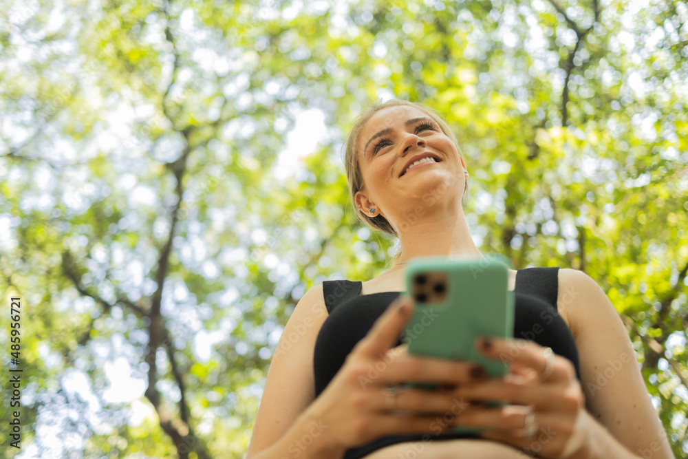 Young woman using a smartphone at day time with a green park in the background. High quality photo