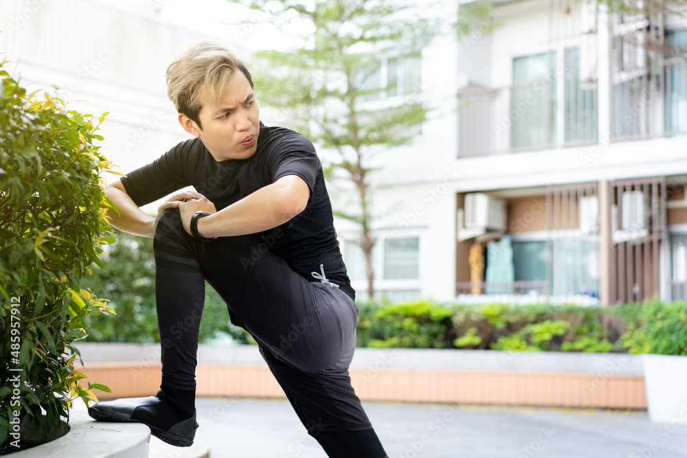 Happy Asian young sportsman doing a lower and upper body stretching before making an exercise in a park. Happy Asian young sportsman doing a lower and upper body stretching before making an exercise in a park.