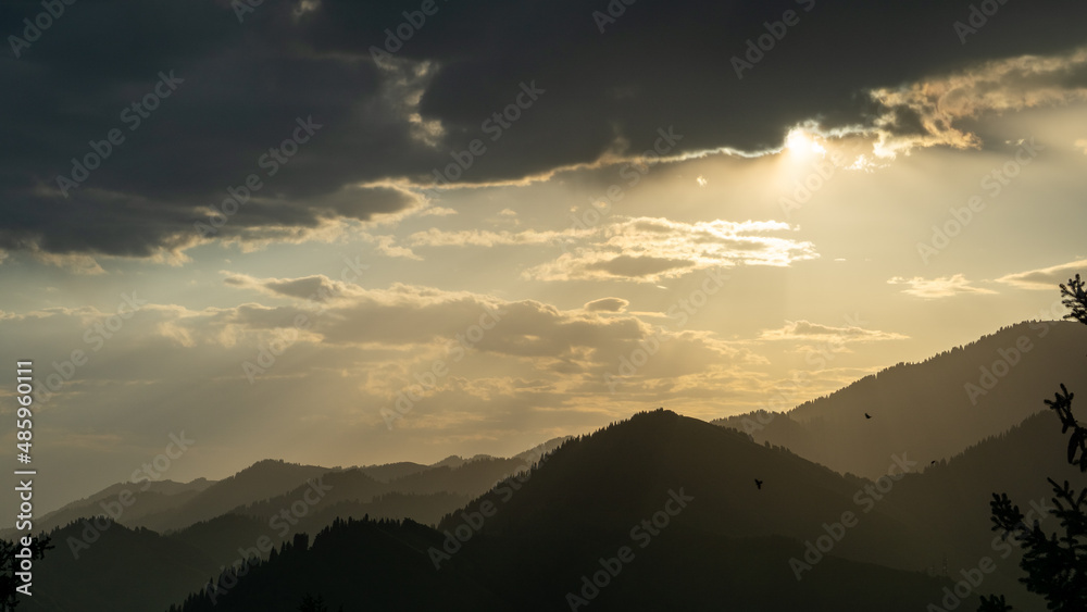 Cloudy dawn over the mountains. The rays of the rising sun pass through the clouds Cloudy dawn over the mountains. The rays of the rising sun pass through the clouds