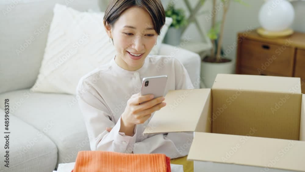 60p　スマホを見ながらダンボールに衣服を入れるミドル女性